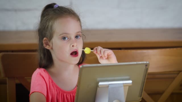 hermosa-niña-comiendo-helado-y-viendo-la-caricatura-en-la-tableta