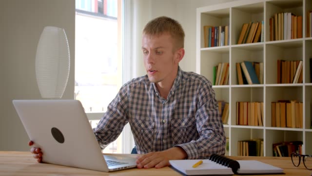 Caucasian-businessman-talking-in-videochat-using-laptop-on-bookshelves-background.