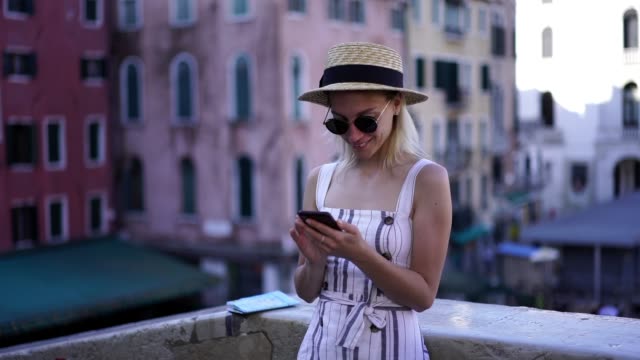 Slow-motion-effect-of-happy-female-tourist-dressed-in-trendy-apparel-using-cellular-phone-for-messaging-with-followers-from-own-travel-blog