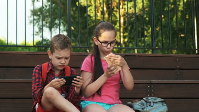 Die-ältere-Schwester-und-der-Bruder-sitzen-auf-der-Straße-und-schauen-auf-Smartphones.