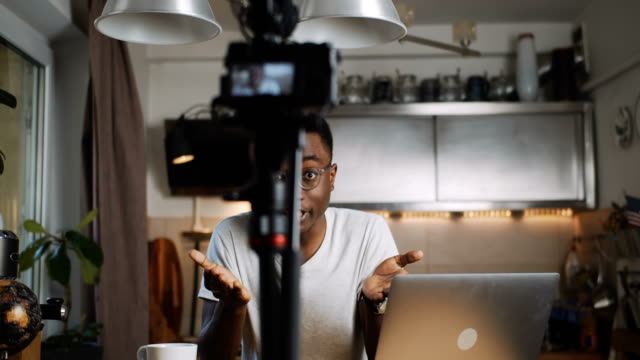 Glücklich-junge-afrikanische-Reise-Blogger-Mann-spricht-Aufnahme-Video-für-Blog-mit-professioneller-Kamera-zu-Hause-Zeitlupe.