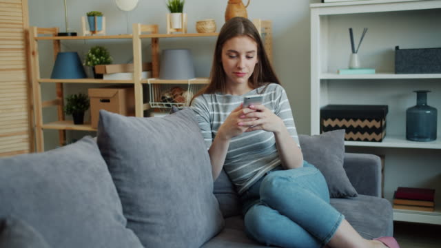 Schöne-junge-Frau-berühren-Smartphone-Bildschirm-auf-couch-im-Haus
