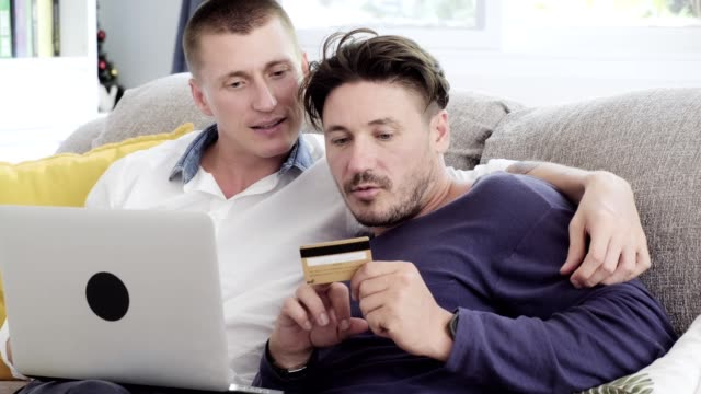 Schwules-Paar-entspannen-auf-der-Couch-mit-Laptop-Computer.-Versuchen-Sie,-die-Kreditkartennummer-anzuzeigen.