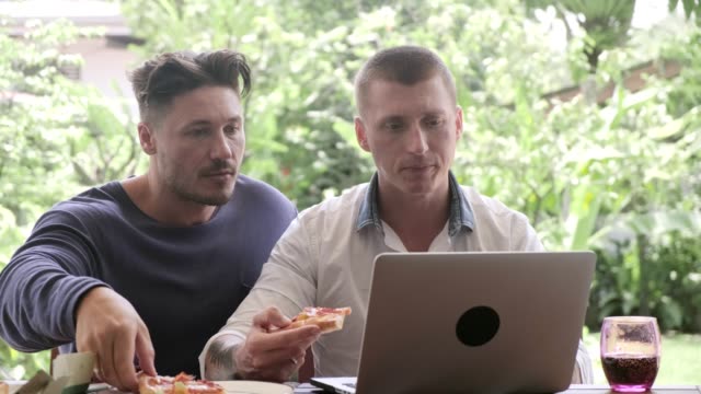 Gay-couple-having-pizza-for-lunch.-Browsing-and-eating-pizza.