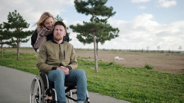 Blonde-Frau-rollt-Rollstuhl-mit-ihrem-behinderten-Freund-im-Freien