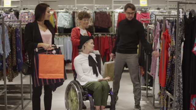 Glückliche-Frau-im-Rollstuhl-und-ihre-Freunde-einkaufen-für-Kleidung