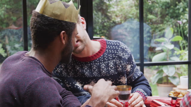 Pareja-masculina-gay-sentada-alrededor-de-la-mesa-para-la-cena-de-Navidad-hablando-y-haciendo-un-brindis