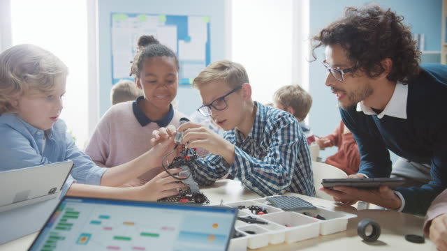 Elementary-School-Robotics-Classroom:-Diverse-Group-of-Brilliant-Children-with-Enthusiastic-Teacher-Building-and-Programming-Robot.-Kids-Learning-Software-Design-and-Creative-Robotics-Engineering