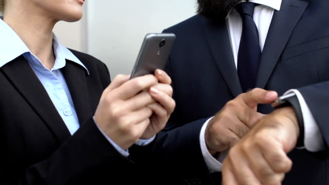 Gerente-femenino-de-desplazamiento-smartphone-al-aire-libre,-colega-masculino-apuntando-al-reloj