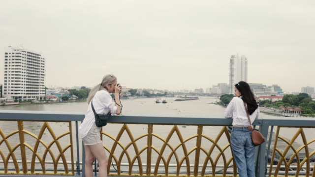 Dos-chicas-parejas-lesbianas-asiáticas-disfrutando-viajando-en-Tailandia-y-usando-una-cámara-de-cine-tomando-una-foto.-Hermosas-mujeres-jóvenes-divirtiéndose-en-el-tiempo-de-vacaciones.-Concepto-LGBT.