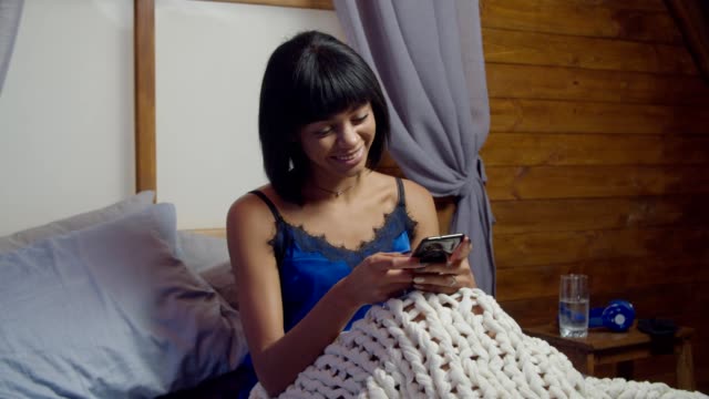 Positive-female-networking-with-smartphone-in-bed