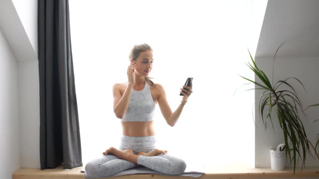 Woman-sitting-on-window-sill-watching-videos-on-smartphone-and-headphones