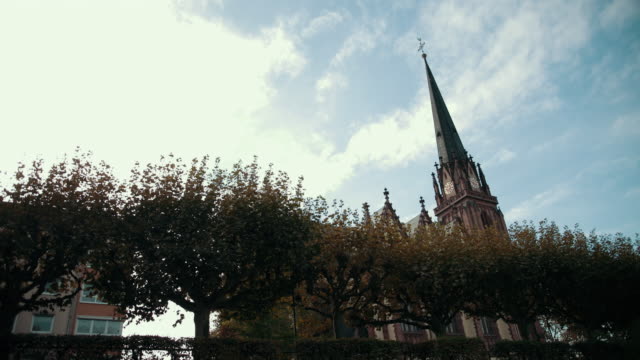 Alte-Kirche-im-gotischen-Stil.-Mit-spitzem-Dach-und-Uhr.-Im-Vordergrund-stehen-Bäume