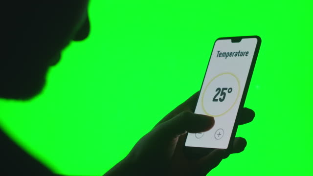 Die-Hand-steuert-die-Smart-Home-App-mit-einem-Smartphone-auf-grünem-Chromakey-Hintergrund