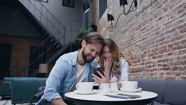 Schöne-fröhliche-Bart-Mann-aufrichtig-lachen-mit-seiner-hübschen-blonden-Freundin-während-Revision-lustige-Video-auf-ihrem-Handy