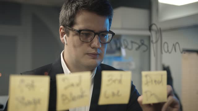 Young-boss-businessman-writing-plans-on-the-sticky-notes-on-glass-wall