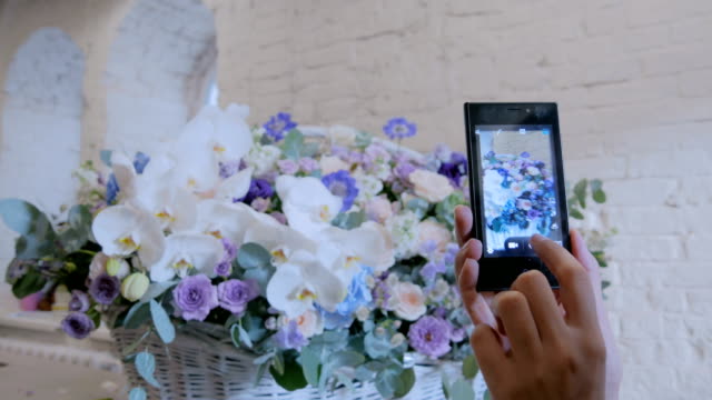 Frau-nehmen-Foto-von-großen-Blumenkorb-mit-Blüten-mit-Smartphone.
