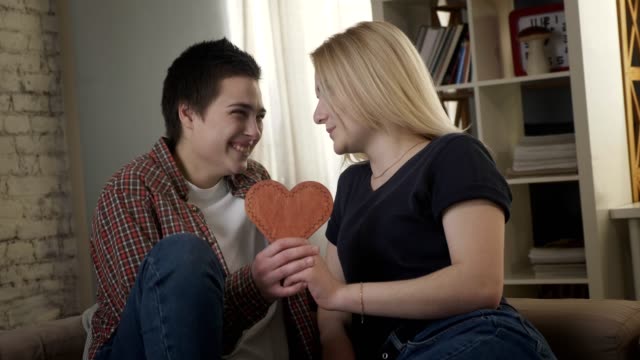 Zwei-junge-Lesben-süß-schauen-einander,-mit-einem-Herzschild-in-der-Hand.-60fps