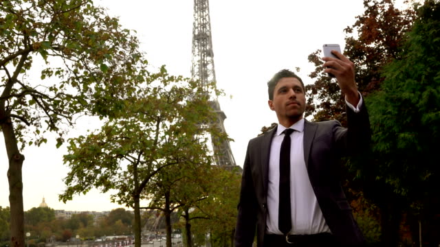 Attraktiver-Mann-in-einem-Anzug-nimmt-ein-Selbstporträt-auf-einem-Smartphone-neben-dem-Eiffel-Turm