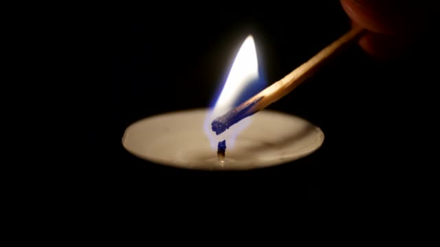 Close-up-of-a-match-lighting-a-candle-against-a-black-background