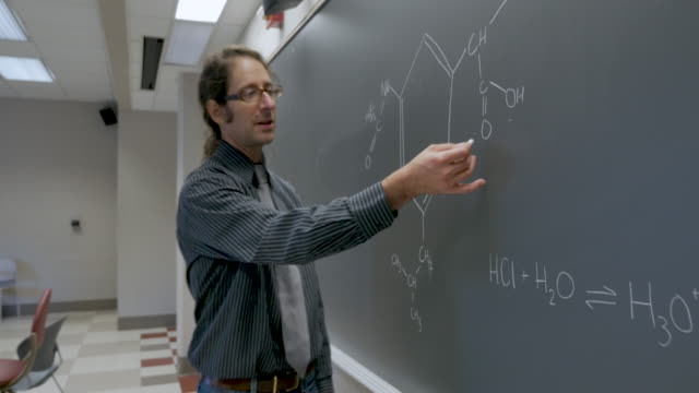 Teacher-writing-on-a-blackboard-using-chalk-teaching-chemistry---stabilized-shot