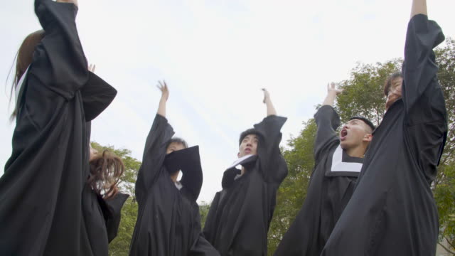 happy--students-in-graduation-gowns-holding-diplomas-on-university-campus