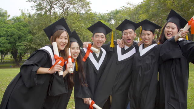glückliche-Studenten-in-Abschlusskleidern-mit-Diplomen-auf-dem-Universitätscampus