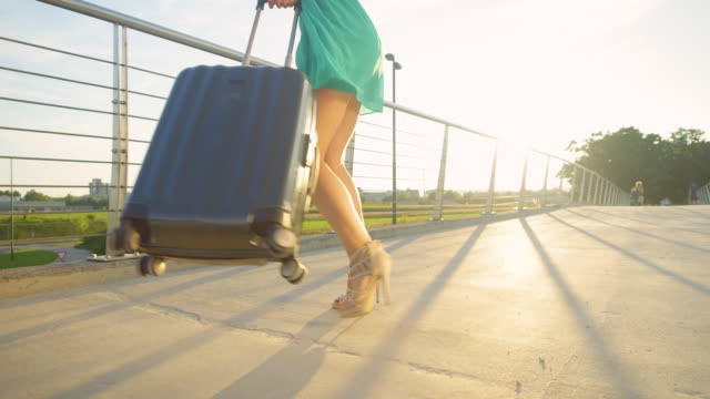 BAJO-ANGLE:-La-mujer-feliz-gira-con-su-maleta-mientras-camina-hacia-el-aeropuerto.