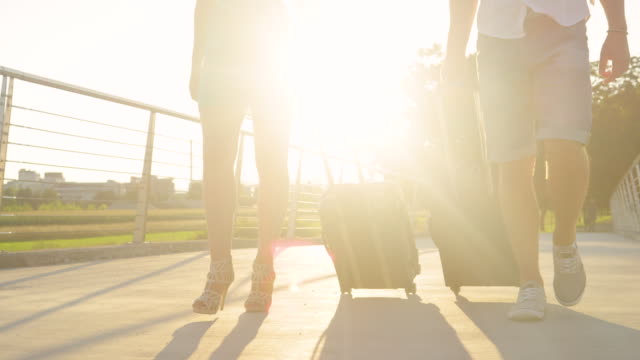 LENS-FLARE:-Goldenes-Licht-leuchtet-auf-Touristenpaar-ziehen-Koffer-hinter-sich.