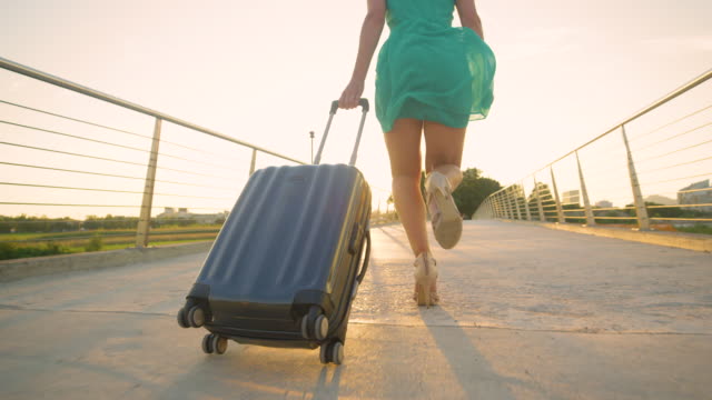 LOW-ANGLE:-Young-woman-in-heels-runs-with-her-luggage-to-reach-airport-on-time.