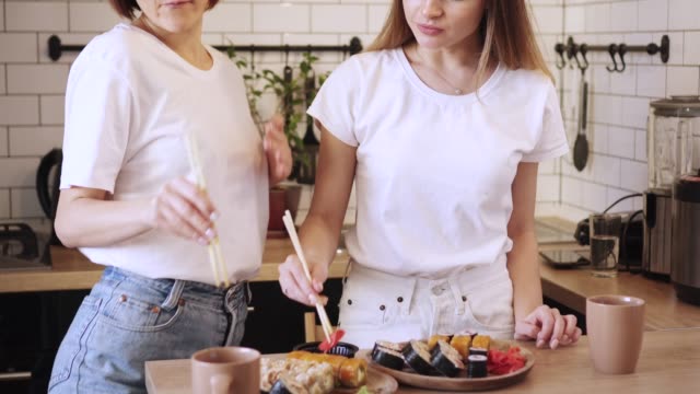 Zwei-lustige-junge-Lesben-essen-Sushi-Rollen-zu-Hause.