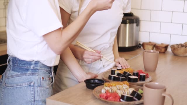 Zwei-lustige-junge-Lesben-essen-Sushi-Rollen-zu-Hause.
