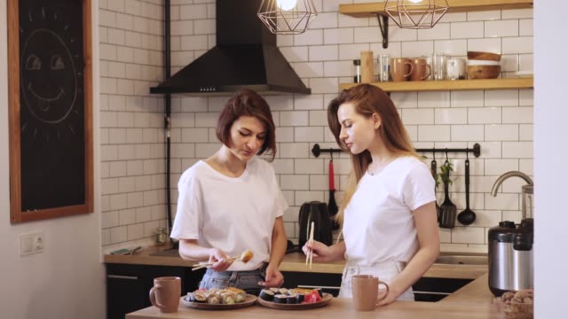 Two-funny-young-lesbians-eat-sushi-rolls-at-home.