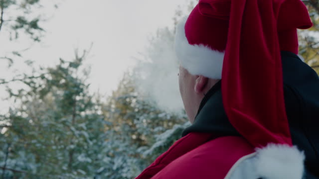 Hombre-en-sombrero-rojo-de-Navidad-fumando-en-el-bosque-nevado-de-invierno.-Hombre-vista-trasera-con-sombrero-de-Año-Nuevo-como-Santa-Claus-fumando-en-el-bosque-de-invierno.