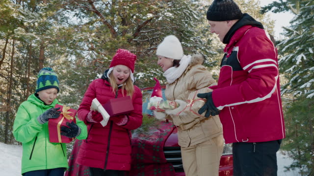 Happy-family-checking-New-Year-gifts-in-snowy-forest-at-winter-walk.-Cheerful-daughter-opening-box-with-Christmas-gift-on-forest-walk.-Happy-New-Year-and-Christmas.