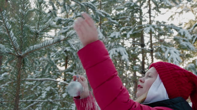 Junge-Frau-hängen-Silberkugel-auf-Neujahr-Baum-Zweig-in-verschneiten-Wald.-Glückliches-Mädchen-Teenager-schmücken-Weihnachtsbaum-mit-Ball-im-Winterwald.