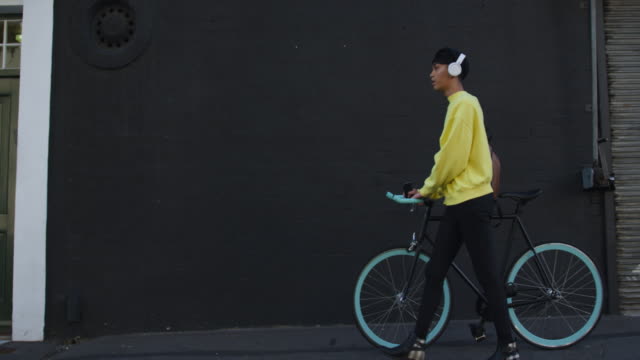 Transgender-adult-walking-with-a-bike-and-using-headphones