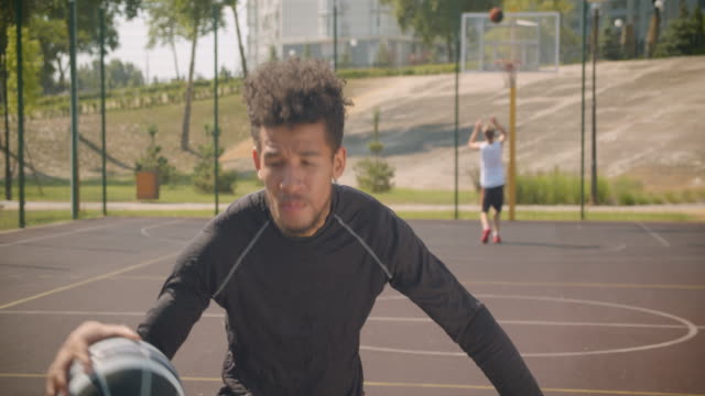Nahaufnahme-Porträt-von-jungen-sportlichen-afrikanischen-amerikanischen-männlichen-Basketballspieler-werfen-einen-Ball-in-einen-Reifen-im-Freien
