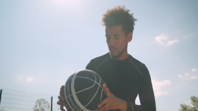 Retrato-de-primer-plano-de-joven-experto-jugador-de-baloncesto-afroamericano-masculino-lanzando-una-pelota-en-un-aro-al-aire-libre