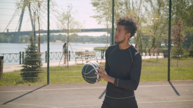 Retrato-de-vista-lateral-de-joven-guapo-jugador-de-baloncesto-masculino-afroamericano-lanzando-una-pelota-en-un-aro-al-aire-libre