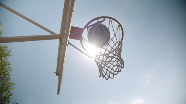 Nahaufnahme-Porträt-von-Basketballball-in-einen-Reifen-im-Freien-auf-dem-Platz-mit-hellem-Sonnenlicht-geworfen