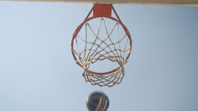 Closeup-bottom-up-view-portrait-of-basketball-ball-being-thrown-into-a-hoop-outdoors-on-the-court-with-sky-on-the-background