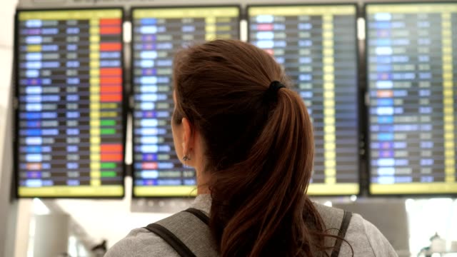 brunette-looks-at-departures-schedule-in-airport-terminal
