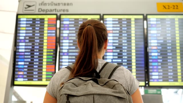 brunette-looks-at-departures-schedule-in-airport-terminal