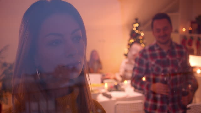 Husband-and-wife-are-smiling-and-parents-are-looking-out-the-window-Christmas-dinner-behind-glass-parents