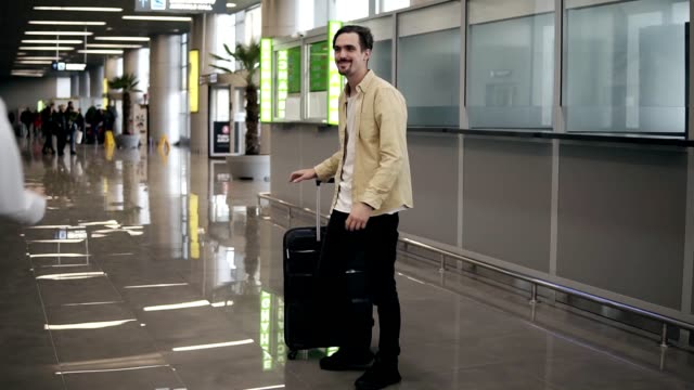 Bearded-young-man-with-suitcase,-waiting-for-his-girlfriend,-in-airport-flying-back-home-from-business-trip-after-long-separation.-Man-hugging-his-girlfriend-and-pick-her-up