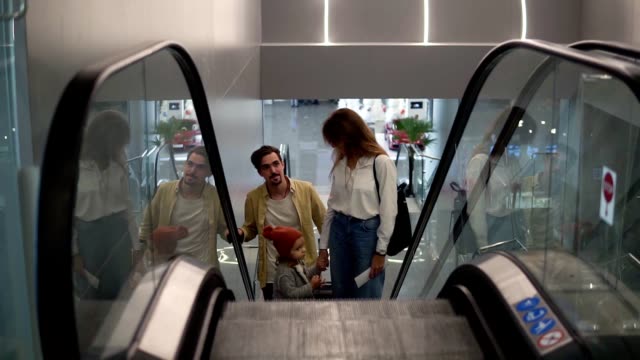 Young-attractive-caucasian-family-with-suitcase-going-up-by-the-escalator-with-their-pretty-daughter-hold-by-mothers-hand-at-the-airport.-Happy-family-vacation-together