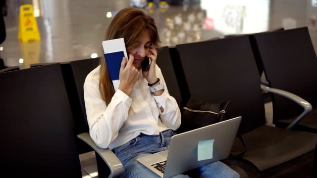 Stylish,pretty-girl-in-white-shirt-uses-phone-and-laptop-to-work-at-airport-while-waiting-boarding-at-departure-lounge.-Talking-to-friends.-Concept-travel,-remote-work