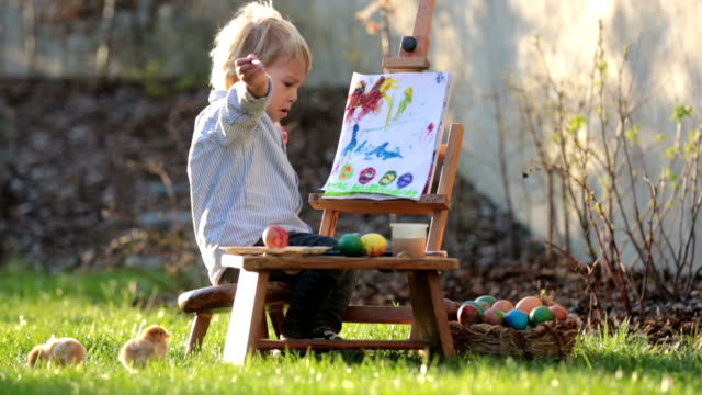 Süßes-Kleinkind-Kind,-Malerei-Eier-im-Garten-mit-kleinen-Küken-um-ihn-herum-bei-Sonnenuntergang-laufen