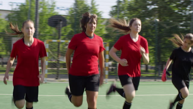 Jóvenes-jugadoras-de-fútbol-femeninos-haciendo-levantamiento-de-talón-corriendo